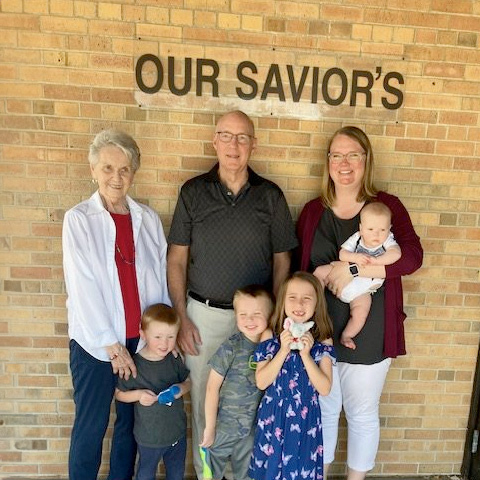 Group of adults and children standing in front of the Our Savior's Lutheran church.